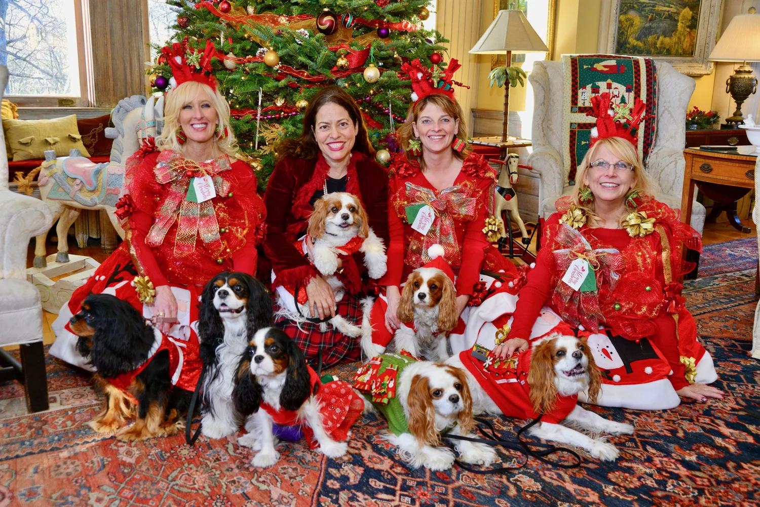 a group of women in red and white with dogs in front of a christmas tree