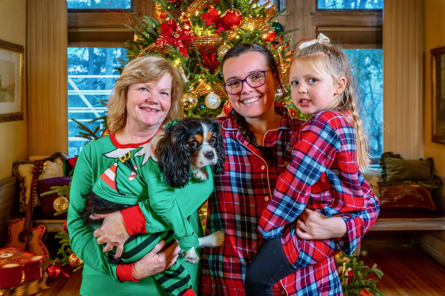 a man and a woman holding a dog in front of a christmas tree